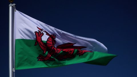 4K: Wales Flag flying in the wind outdoors with Blue sky behind - Welsh flag on flagpole. Stock Video Footage