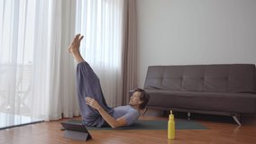 A young man at home doing yoga following instructions from a video he watches on a tablet. Social distancing concept. Internet trainer concept