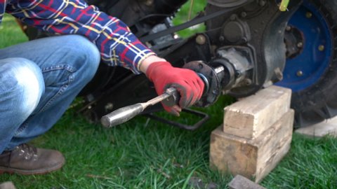 knock out a wedge from a tractor shaft,a man repairs a tractor, a hammer to knock out a maple on the shaft of a two-wheeled tractor