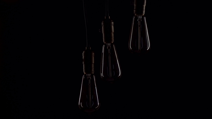 Three retro lamps hang and turn on at the same time on black background. Antique bulbs with old lamp holder are switched on Royalty-Free Stock Footage #1054408553