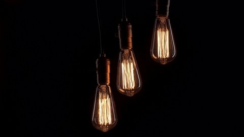 Three retro lamps hang and turn on at the same time on black background. Antique bulbs with old lamp holder are switched on