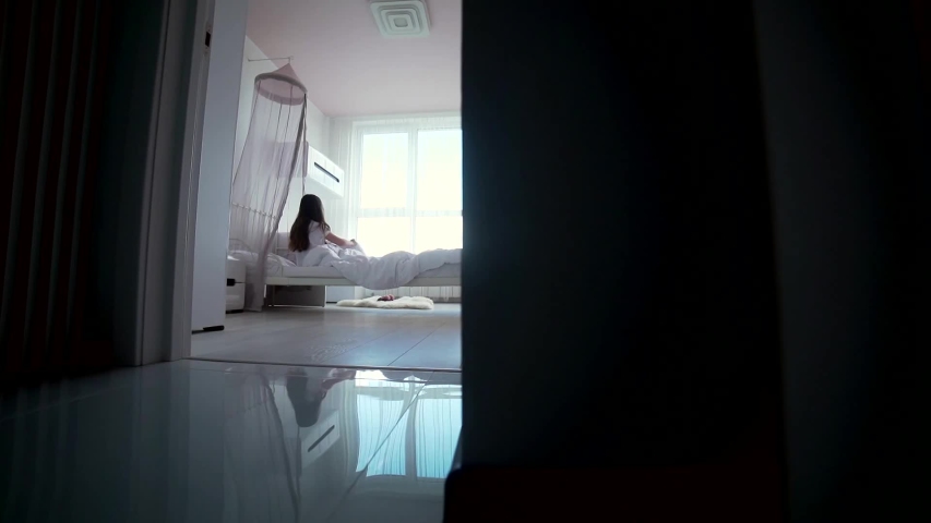 little teen girl wakes up in the morning in the bedroom gets up comes to the window and pulls his hands up. silhouette child through the door getting out of bed morning. quiet cozy children room	 Royalty-Free Stock Footage #1054408676