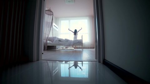 little teen girl wakes up in the morning in the bedroom gets up comes to the window and pulls his hands up. silhouette child through the door getting out of bed morning. quiet cozy children room	