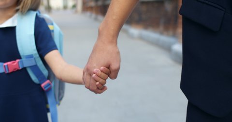 Close up view of mother and daughter walking hand in hand together at street. Mom taking her elementary graded kid to school. Concept of family relationships