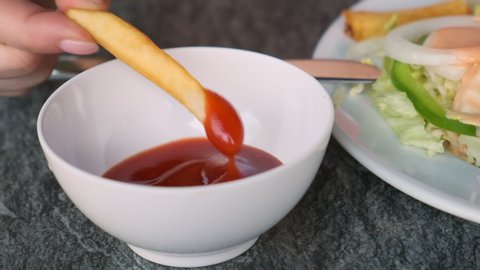 French fries female hand dips in sauce closeup.