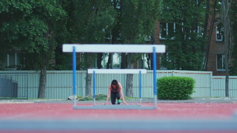 Caucasian female athlete practicing at a sports stadium, hurdling on running track, slow motion. Track and Field Sports Training in Stadium.