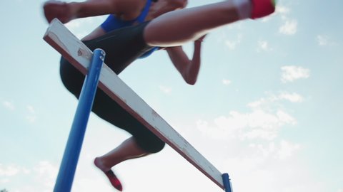 Caucasian female athlete practicing at a sports stadium, hurdling on running track, slow motion. Track and Field Sports Training in Stadium.