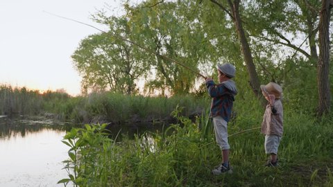rural weekend, happy carefree boys enjoying nature and fishing with a fishing rod on river bank among trees and setting sun while relaxing in countryside