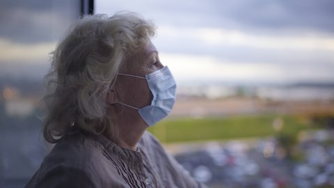 Senior woman wearing protective face mask, looking at city, epidemic lockdown