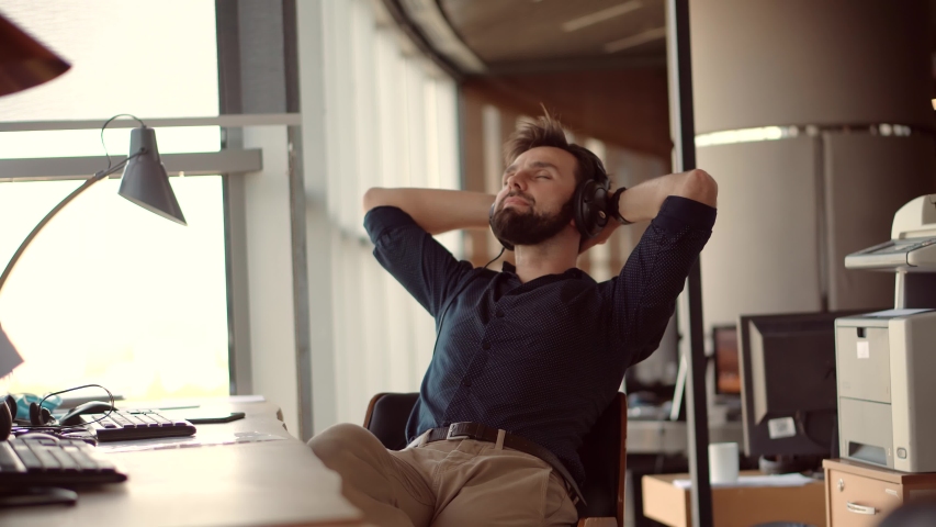 Thoughtful Serious Man Sitting On Workplace And Listening Podcast.Happy Healthy Stress Free Man Relaxing In Office And Listening To Music.Employee Taking Break On Work.Businessman Leisure In Headphone Royalty-Free Stock Footage #1054416383
