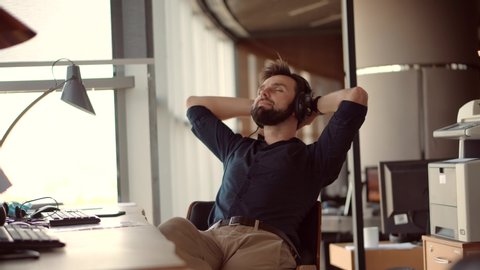 Thoughtful Serious Man Sitting On Workplace And Listening Podcast.Happy Healthy Stress Free Man Relaxing In Office And Listening To Music.Employee Taking Break On Work.Businessman Leisure In Headphone