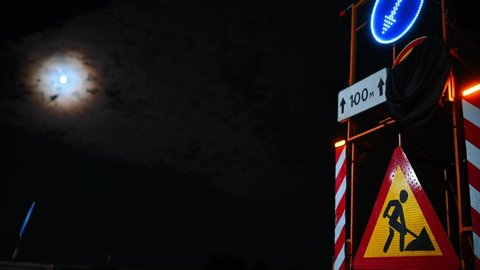 Repair work is underway on the road at night. Sign on the road. Night road works time lapse moon