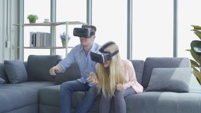 A western young couple wearing VR or virtual reality glasses, headsets sitting and playing a video game on sofa in front of TV at home in technology and innovation concept. Having fun. Entertainment