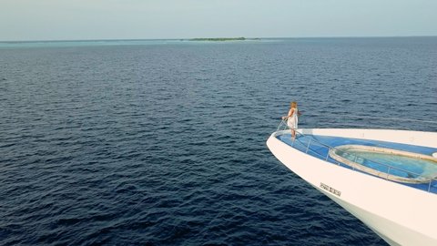 Drone spins around woman standing on deck of big private white yacht. Incredible inspiring romantic getaway concept. Inner peace and self love, self care vacation in tropical destination