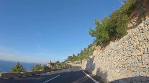 4K point of view footage of car driving on winding road along the coast of Mediterranean sea, pine trees, cliffs and beautiful mountain landscape. Spring on Mallorca island, Spain. Slow motion video