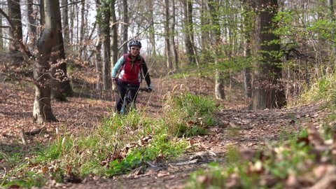 nice senior woman riding her electric mountain bike on a forest trail in early spring