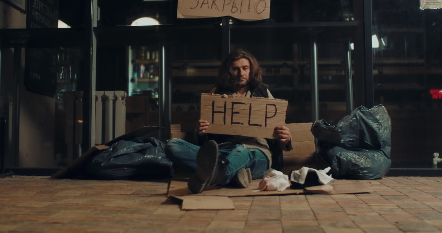 Homeless bum night city. Joblessness vagabond looking at camera help sign poverty 4K. Destitute man begging on street financial crisis jobless. Homelessness poor emigrant tramp. Destitution vagabonds. | Shutterstock HD Video #1054424678