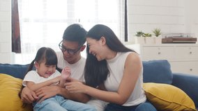 Happy cheerful Asian family dad, mom and daughter having fun cuddling playing on sofa while birthday at house. Self-isolation, stay at home, social distancing, quarantine for coronavirus prevention. - Powered by Shutterstock - Get 15% off with code: PIKWIZARD15