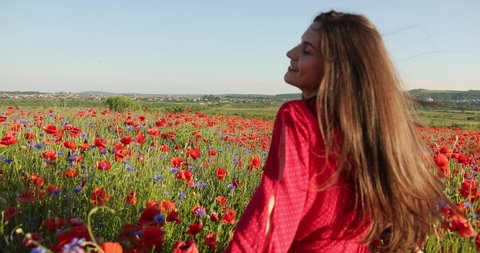 Pretty woman run in a red field of flowers and touches by her hands poppy. Young beautiful woman with charming smile. Portrait view. 4K. Beautiful landscape
