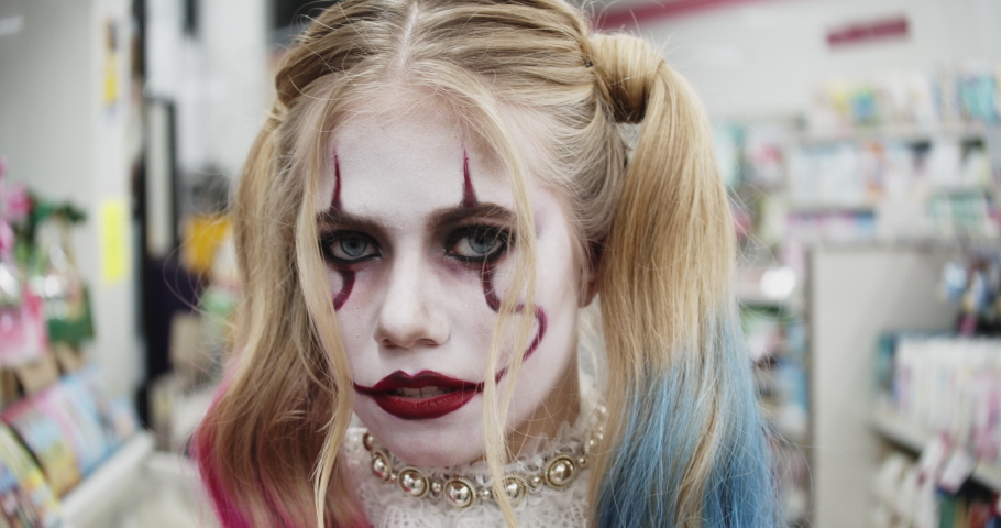 Headshot of a female cosplayer dressed as Harley Quinn as she stares at the camera and winks; grocery store in the background. Royalty-Free Stock Footage #1054426424