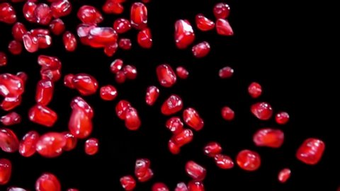 Ripe pomegranate grains are flying diagonally on a black background in slow motion, loop footage