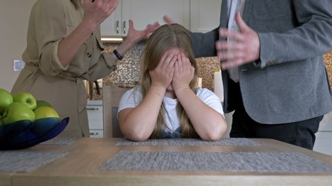 Problems of parenting in the family. Parents very much scolding a teenage daughter for something. They scream at the child. The girl helplessly covered her face with her hands.