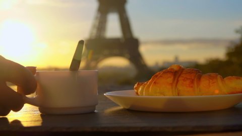 Hand takes a cup of morning coffee with freshly baked croissant on the background of the Eiffel Tower, Paris, France