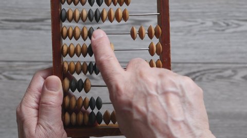 A Elderly Man Is Holding And Moves Wooden Knuckles On A Outdated Vintage Wooden Abacus On A Gray Background, Close-up. .