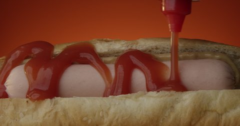 Hot Dog Closeup with Ketchup Pouring on Hotdog with Sausage and Mustard Against Terracotta Background a Profile Studio Shot