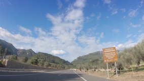 4K POV footage of car driving on highway road. Blue sky and beautiful mountain landscape. Olive plantations and flowering almond gardens on the sides. Spring on Mallorca, Sierra de Tramontana 
