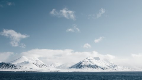 Long shot of snow covered mountains in Svalbard, and a single bird in the sky.