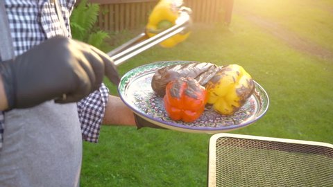 Hand of young man grilling vegetables on the barbecue plate with glowing coals, summer picnic time, bbq grill with fire in garden, vegan food and healthy eating outdoor fresh tasty food concept