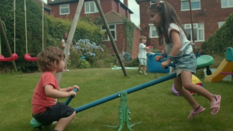 Young boy and girl playing on a seesaw in a garden.