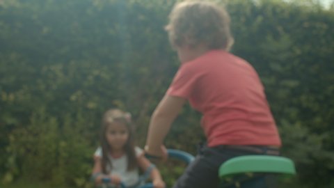 Young boy and girl playing on a seesaw in a garden.