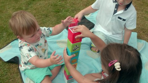 Group of young children sitting on blanket in garden, playing with building blocks