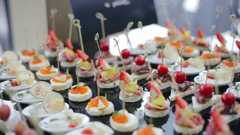 Appetizing and delicious wedding snacks on skewers for guests, such as strawberries, cherries, brie cheese, red caviar, pineapple, lemon on a black table tray in the morning at the banquet hall.
