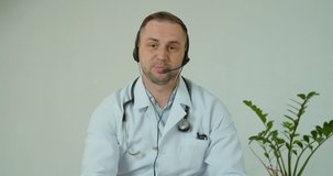 Professional male doctor in white medical coat and headset making conference call on laptop computer, consulting distance patient online in video chat, explain treatment by webcam concept.