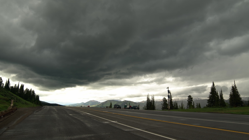 Dark dramatic storm moving over road on mountain summit in Wyoming as vehicles travel on the highway.