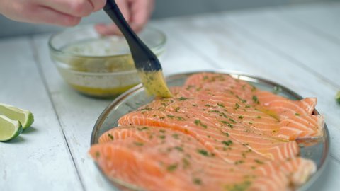Close-up of brushing raw salmon with marinade sauce using a basting brush. Fillets of salmon being brushed with melted butter, garlic, greens. Concept of preparing salmon for cooking on the grill.