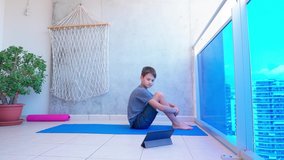 Boy doing sport exercises while watching video lesson online on tablet computer on balcony. Sport, healhty lifestyle, active leisure at home