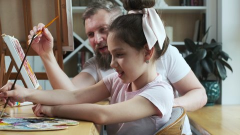 Dad advising his little girl how to paint. Father's day for father and daughter: painting pictures. Young bearded caucasian father and his child spending quality time together on special day.