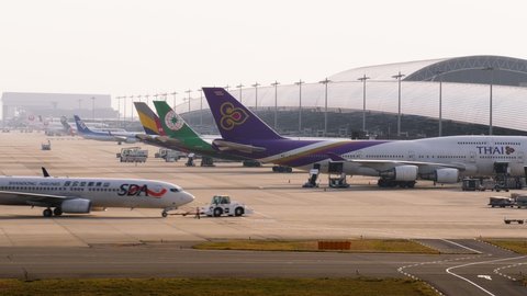 OSAKA, JAPAN - APRIL 07, 2018: Airliners parked at passenger terminal gates, one plane finish boarding and pushed back to taxiway by small tug. Time lapse shot of Kansai International Airport