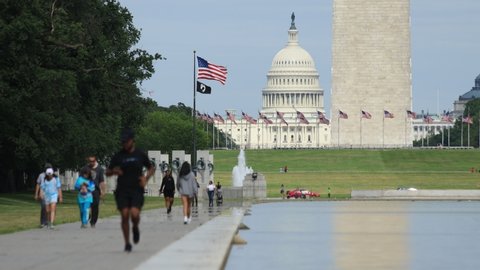 Washington, DC / United States - June 16 2020: Pedestrians walk alongside the reflecting pool. The base of the Washington monument and the U.S. Capitol Dome are seen in the background