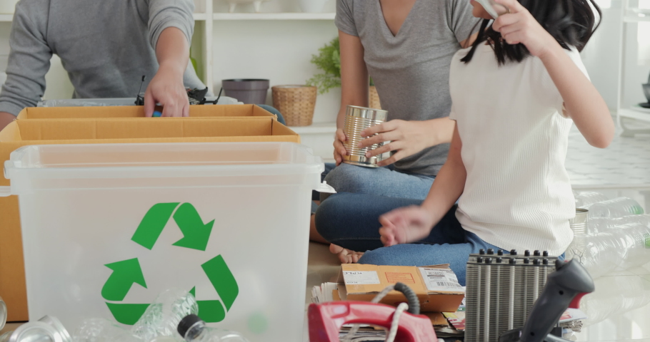 Little girl and her family helping to separate plastic bottle into recyclable bin at home together.