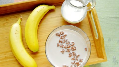Ready-made Breakfast cereal with chocolate letters alphabet muesli, hand stirs the milk and cereal with a spoon in a bowl. Two bananas, a jug of milk on a wooden tray, healthy food, top view