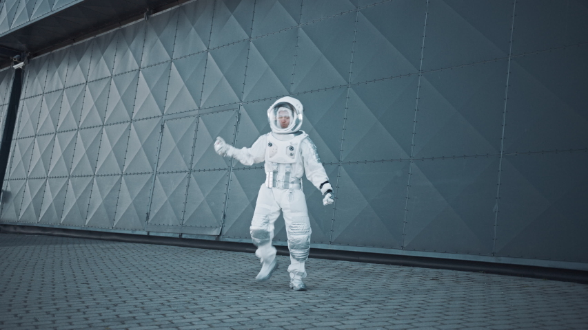 Handsome Man in Spacesuit is Dancing Next to Metal Wall. Astronaut is Happy and Makes Creative Robotic Moves. Successful Spaceman in White Futuristic Suit with Technological Panel on His Hand. Royalty-Free Stock Footage #1054464440