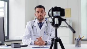 healthcare, medicine and blogging concept - male doctor with camera recording video blog at hospital