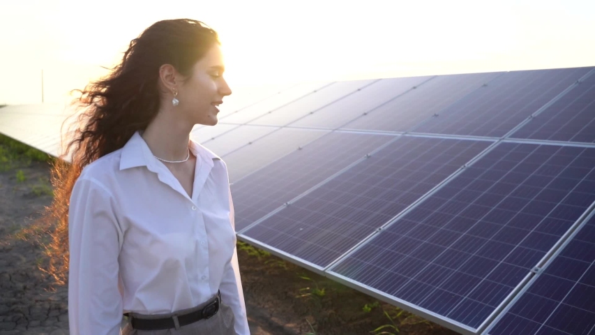 Woman walks near solar panels row on the ground at sunset and touch solar cells. Woman investor wears formal white shirt. Free electricity for home. Sustainability of planet. Green energy. Royalty-Free Stock Footage #1054470566