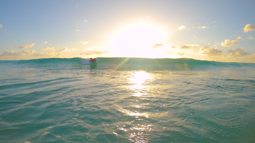 SLOW MOTION, LENS FLARE: Cinematic shot of a female beginner surfer riding a small wave to the tropical coast at sunset. Woman learning to surf stands up on her longboard and rides a wave at sunrise. | Shutterstock HD Video #1054471790