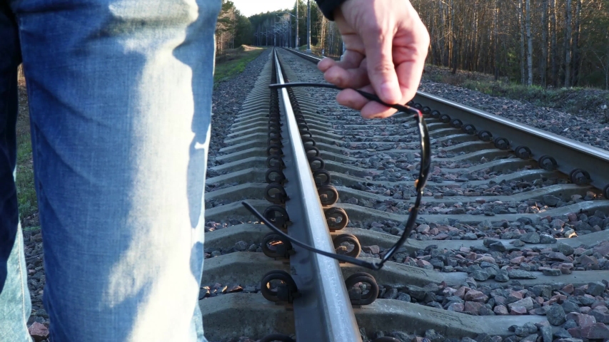 A man holding sunglasses in his hands on a rail background. Railroad rails and glasses in the hands of a man.